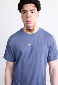 Marineblå bomulls t-skjorte med korte ermer, med en liten neongrønn Nike-logo på brystet. Glatt tekstur, klassisk rund halsdesign.