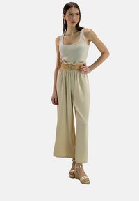 Beige tanktop met gerimpelde halslijn, gedragen met beige wijde broek en een gevlochten riem met een ronde gesp. Gouden wedge sandalen.