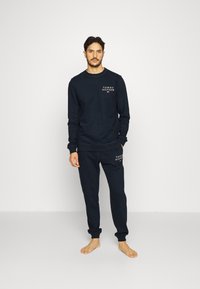 Ensemble de sweatshirt et pantalon de survêtement en coton bleu marine avec des impressions de logo sur la poitrine et la cuisse. Bords-côtes au niveau des poignets et des chevilles. Design minimal.