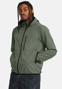 Chaqueta verde con capucha, cierre frontal, acentos negros contrastantes, bolsillo en el pecho y puños elásticos. Tejido suave y ligero.