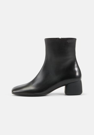 Mustat nahkaiset nilkkasaappaat, joissa on pyöreä kärki, vetoketjukiinnitys ja paksu musta korko. Sileä pinta ja minimalistinen muotoilu.