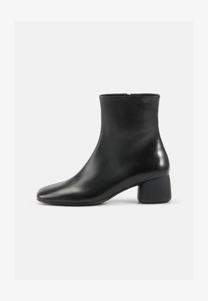 Bota curta em couro preto com bico arredondado, fecho de correr e salto largo preto. Superfície lisa e design minimalista.