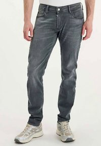 Vaqueros ajustados de mezclilla gris con sutil desgaste, cierre de botones, diseño de cinco bolsillos y resistentes zapatillas deportivas de color gris claro.