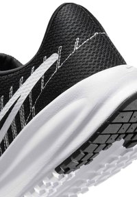 Gros plan sur le talon d'une chaussure de sport noire et blanche avec semelle texturée et détails de coutures blanches sur une tige en tissu respirant.