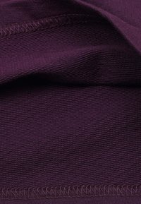 Nahaufnahme von strukturiertem lila Stoff mit sichtbaren Nähten entlang der gefalteten Kanten.