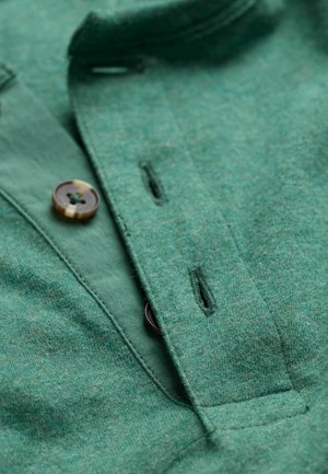 Green textile shirt featuring a soft texture, button closures, and a collar. The fabric shows a subtle heather pattern with contrasting buttons.