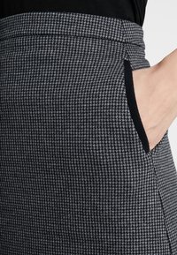 Kangas houndstooth-kuviolla mustavalkoisena, jossa on istuva vyötärö sivutaskuilla ja sileä rakenne.