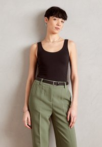 Crna majica bez rukava u kombinaciji s hlačama visokog struka u maslinastozelenoj boji. Outfit sadrži crni pojas i jednostavne srebrne nakitne detalje.