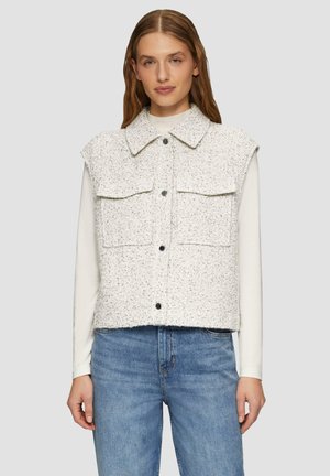 Gilet sans manches en tweed blanc avec deux poches avant et fermeture à boutons. Présente un col pointu et un tissu texturé. Porté par-dessus une chemise à manches longues.
