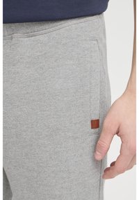 Grå sweatpants fremstillet af blødt stof, med en sidelomme og en detalje med en brun læder标签. Ribbet talje for ekstra komfort.