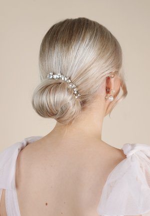 Haarschmuck mit einer silberfarbenen Haarspange, besetzt mit klaren Strasssteinen, gestylt in einem tiefen Dutt, mit weichem blonden Haar und einem transparenten weißen Schulterdetail.
