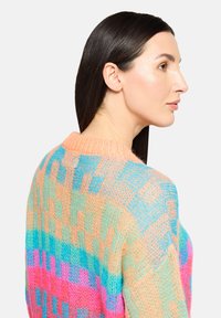 Pull en maille coloré avec un motif géométrique rose, bleu et orange. La texture est douce et en maille ajourée avec un col rond.