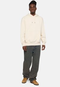 Felpa con cappuccio di colore beige chiaro, realizzata in un materiale morbido con una tasca frontale. Abbinate a jeans in denim blu scuro a vestibilità morbida e sneakers marroni.