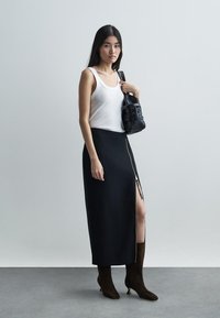 Fekete szoknya oldalsó cipzárral, fehér topal párosítva. Barna velúr térd fölé érő csizma és egy kis fekete kézitáska. Semleges háttér.
