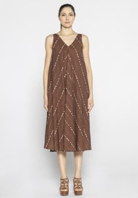Brązowa, bezrękawnikowa sukienka z dekoltem w kształcie V, z nieregularnymi, białymi ukośnymi paskami. Krój ma luźny fit, sięgający do kolan.