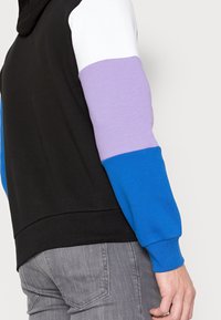 Felpa con cappuccio caratterizzata da un corpo nero e maniche con blocchi di colore bianco, viola e blu. Realizzata in morbido cotone misto con polsini a coste.