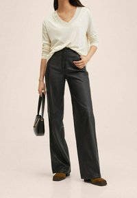 Pantalons larges noirs en simili cuir, associés à un pull crème à col en V. Accessoirisés avec un petit sac à main noir et des bottes à talons marron.