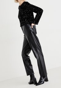 Haut à manches longues en sequins noirs associé à un pantalon en faux cuir noir à motif crocodile et des bottines noires à talon carré.