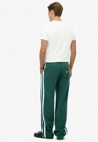 Groene joggingbroek met witte zijkanten, losse pasvorm en een achterzak. Gecombineerd met een basic witte T-shirt met korte mouwen.