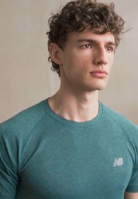 Camiseta atlética en color teal con mangas cortas, que presenta una textura sutil y un pequeño logo blanco de "N" en el lado izquierdo del pecho.