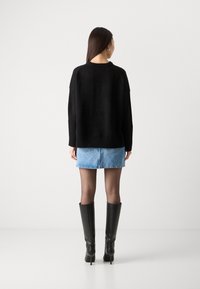 Černý oversized svetr s žebrovanými manžetami, světle modrá džínová mini sukně a černé kozačky na vysokém podpatku. Jednoduchá, texturovaná tkanina.