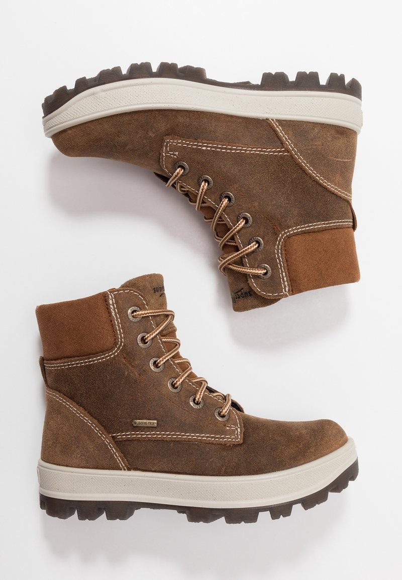 Bottes de randonnée en daim marron avec semelles en caoutchouc blanches et lacets beige, dotées d'un tissu Gore-Tex pour l'imperméabilité et une semelle robuste pour l'adhérence.