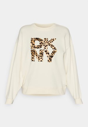 Kreminės spalvos laisvai krentančios sportinės kelnės, su priekinio džemperio piešiniu, kuriame matyti raidės "DKNY" leopardų raštu.