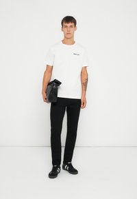 Hvid bomulds t-shirt med "REPLAY" logo i sort, parret med sorte slim-fit bukser og en sort taske. Sko: sorte sneakers med hvide detaljer.