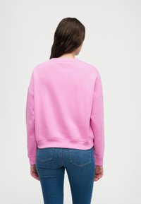 Sweatshirt rose avec un col rond, design à épaules tombantes et poignets côtelés. Associé à un jean bleu ajusté, affichant une coupe décontractée.