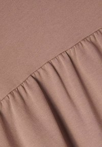 Textureret stof i blød mauve med et plisseret design i bunden, der viser en glat, strikket overflade og sammenfoldet detaljering.