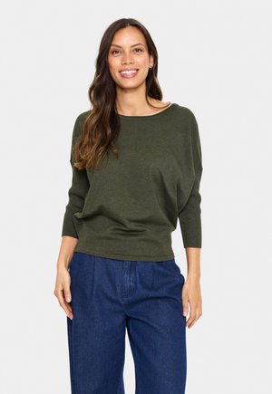Dark green sweater with a wide, round neckline and three-quarter sleeves, paired with loose blue denim pants. Soft texture, relaxed fit.
