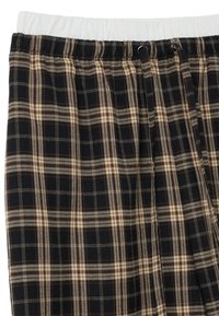 Tissu en tartan noir et beige avec une finition texturée. Comprend une taille élastiquée avec une doublure intérieure blanche et un cordon de serrage pour l'ajustement.