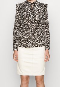 Svart och beige blus med abstrakt mönster, volangaxlar, nyckelhålsringning och långa ärmar, matchad med en krämfärgad blyertskjol.