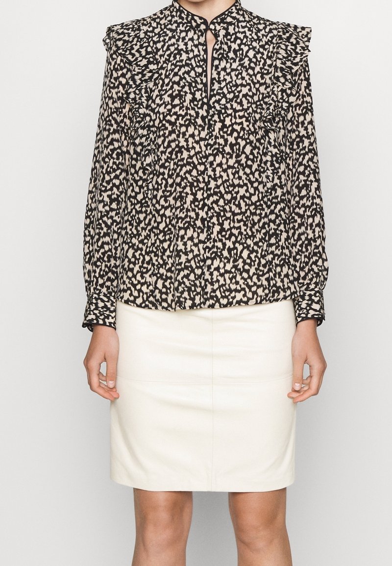 Svart och beige blus med abstrakt mönster, volangaxlar, nyckelhålsringning och långa ärmar, matchad med en krämfärgad blyertskjol.