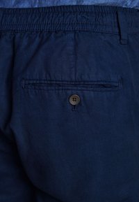 Șorturi bleumarin cu un tiv elastic și o buzunar la spate cu închidere printr-un nasture maro. Material neted cu o strălucire subtilă.