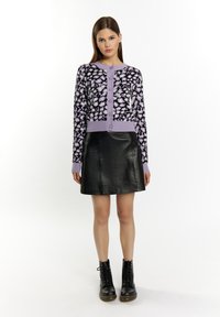 Gonna in pelle nera con forma a A, abbinata a un cardigan a fantasia viola e nera con bottoni e polsini a coste. Stivali neri alla caviglia.