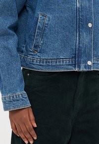 Denim jakna u svijetloplavoj boji s lagano izblijedjelim završetkom, koja ima prednje kopčanje na dugmad, dvije bočne džepove i kontrastne detalje na manžetama.