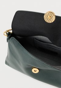 Roheline nahast käekott musta sisuga, millel on tekstuuriga kuldne nööpkinnitusega ja sees olev libistasku.