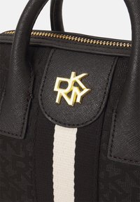Bolso negro con tejido texturizado, herrajes de logotipo dorado y un acento de franjas blancas. Cuenta con dos asas superiores y un cierre de cremallera.