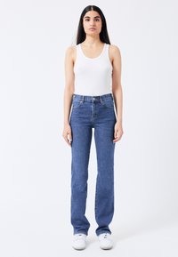 Jeans de mezclilla azul con diseño de cintura alta y pierna recta, combinados con una camiseta sin mangas de rayas blanca y zapatillas blancas.