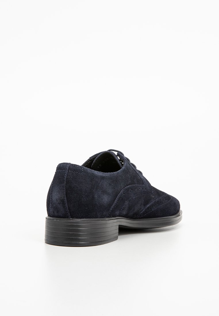 Chaussure oxford en suède marine avec un bout rond, des coutures contrastantes et un petit talon noir. Texture lisse et design classique.