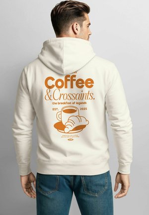Cream-colored hoodie featuring an orange graphic with the text "Coffee & Croissants," a cup, and croissant illustration on the back.