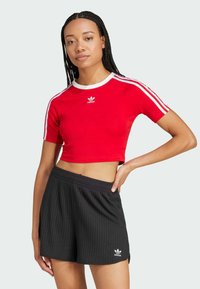 Red cropped t-shirt with white trim and Adidas logo, paired with black ribbed shorts featuring an Adidas logo in white.