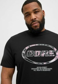 Schwarzes Baumwoll-T-Shirt mit einem kreisförmigen weißen und pinken "CORE"-Grafik. Enthält den Text "JACK&JONES" unter dem Logo, standardmäßig geschnitten.