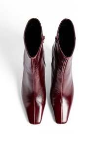 Bottines en cuir bourgogne avec un design élégant, un bout pointu et une fermeture éclair. Texture lisse avec une finition brillante.