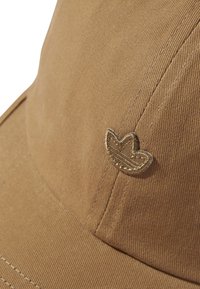 Boné de algodão marrom com tecido texturizado, aba curva e um detalhe com logotipo costurado na frente.