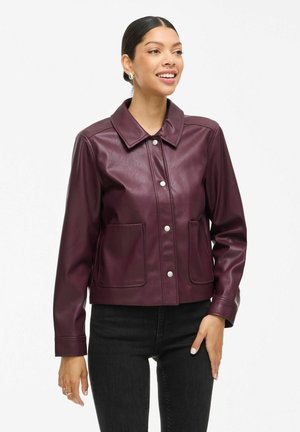 Burgunderfarbene Kunstlederjacke mit kragenförmigem Ausschnitt, Druckknopfverschluss, zwei vorderen Taschen und langen Ärmeln, kombiniert mit schwarzen Jeans.
