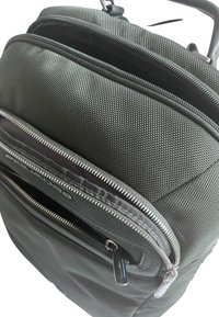 Zaino verde scuro con tessuto testurizzato, molteplici compartimenti con zip e una maniglia resistente. Presenta una zip pull liscia e accenti a contrasto.