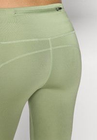 Leggings de sport vert clair en matériau lisse et extensible avec des coutures à plat et une poche zippée à l'arrière.