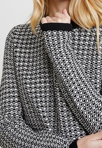 Schwarzer und weißer Strickpullover mit einem strukturierten Muster, gerippten schwarzen Bündchen und einem lockeren Schnitt, der ein gemütliches, geschichtetes Design präsentiert.